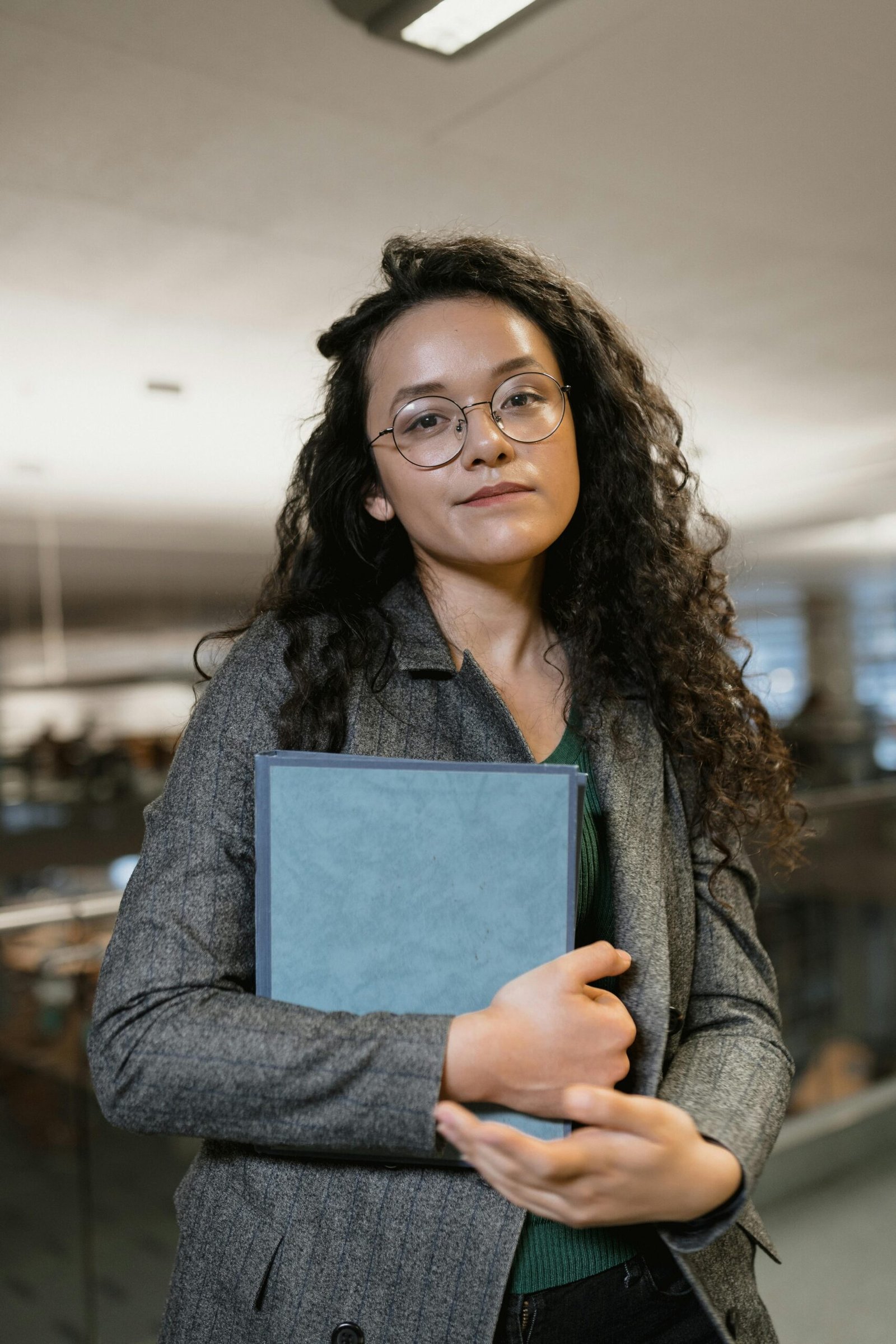 Young woman with eyeglasses holding a book in a stylish indoor library setting.
